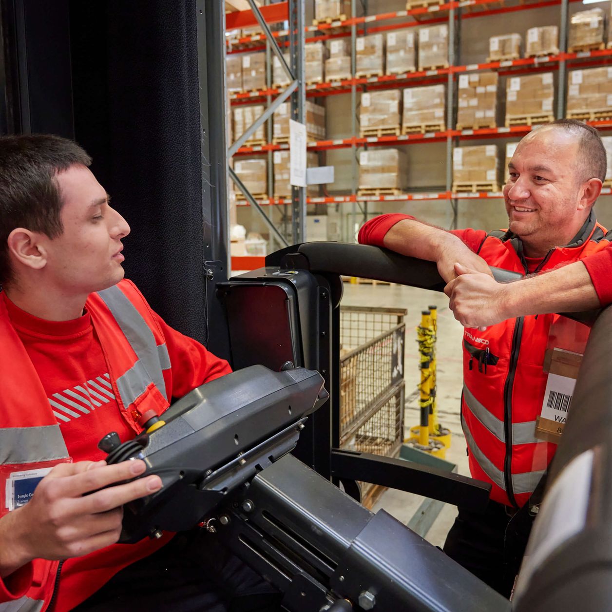 Logistikmitarbeiter in Stapler sitzend im Gespräch in einer Transco Lagerhalle