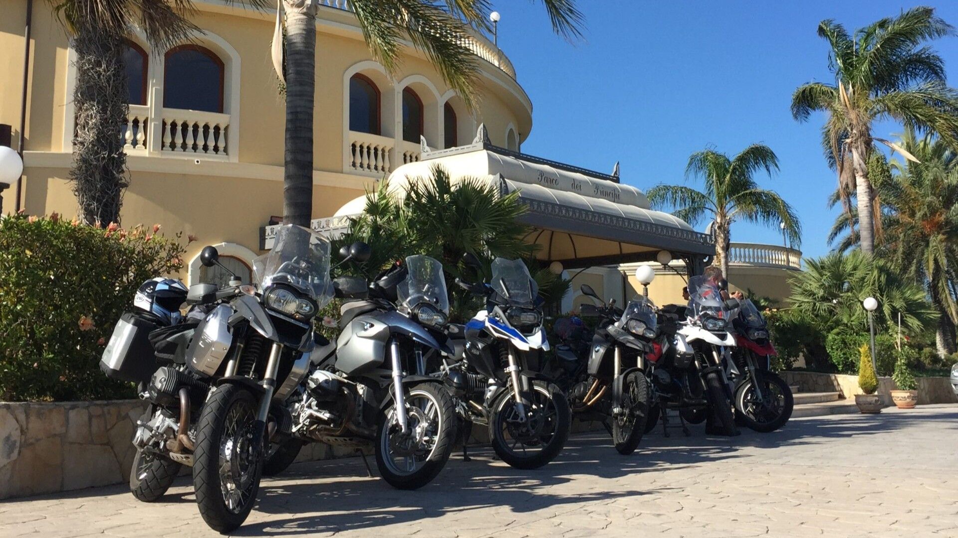 geparkte Motorräder vor einem mediterranen Gebäude und Palmen