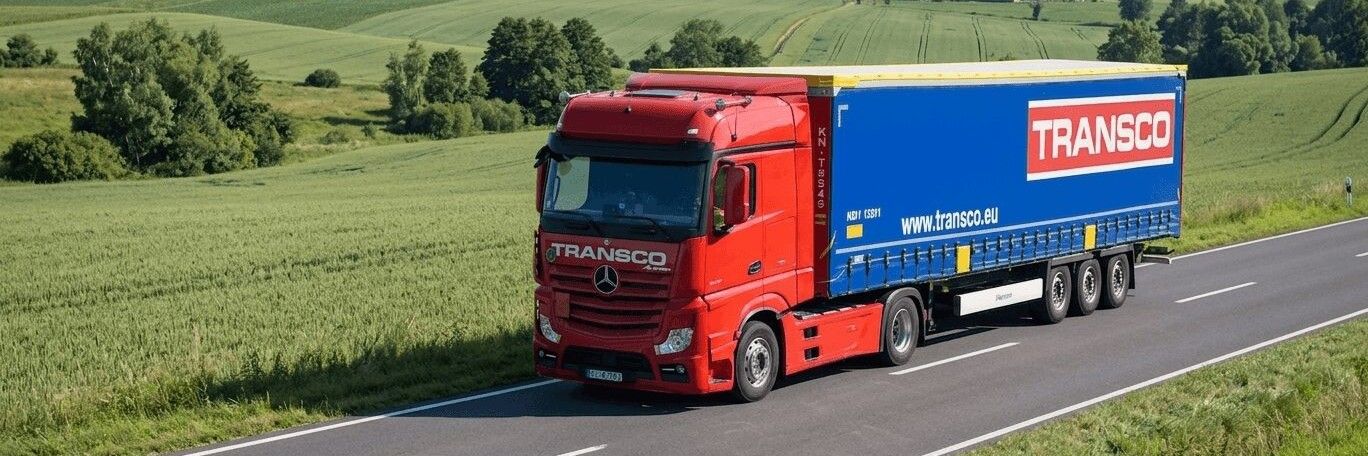 Nákladní vůz přepravní společnosti Transco projíždí zelenou krajinou