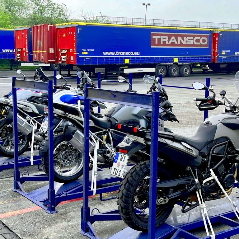 Motorräder in Transportgestellen vor Aufliegern der Spedition Transco