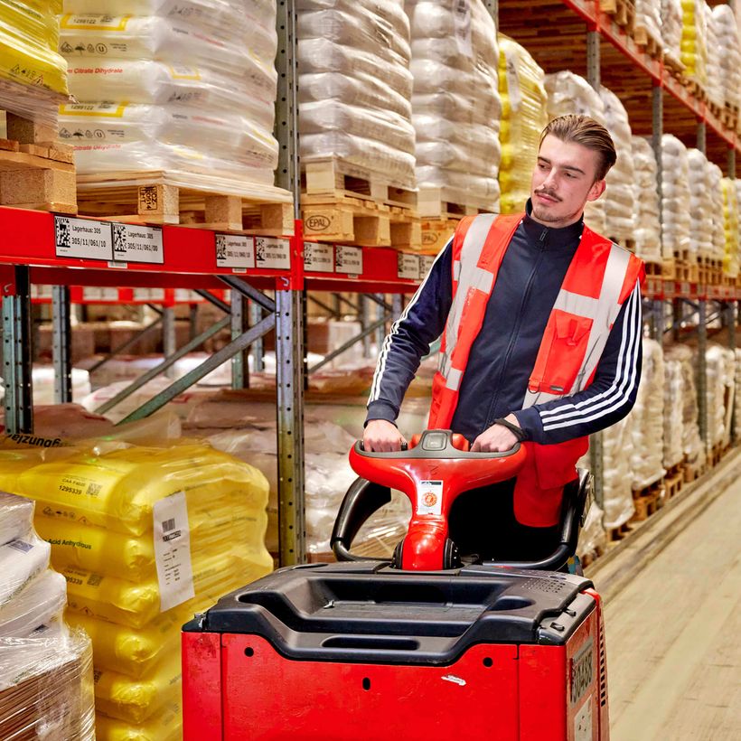 Logistik Mitarbeiter auf Hubwagen vor Hochregallager bei Transco