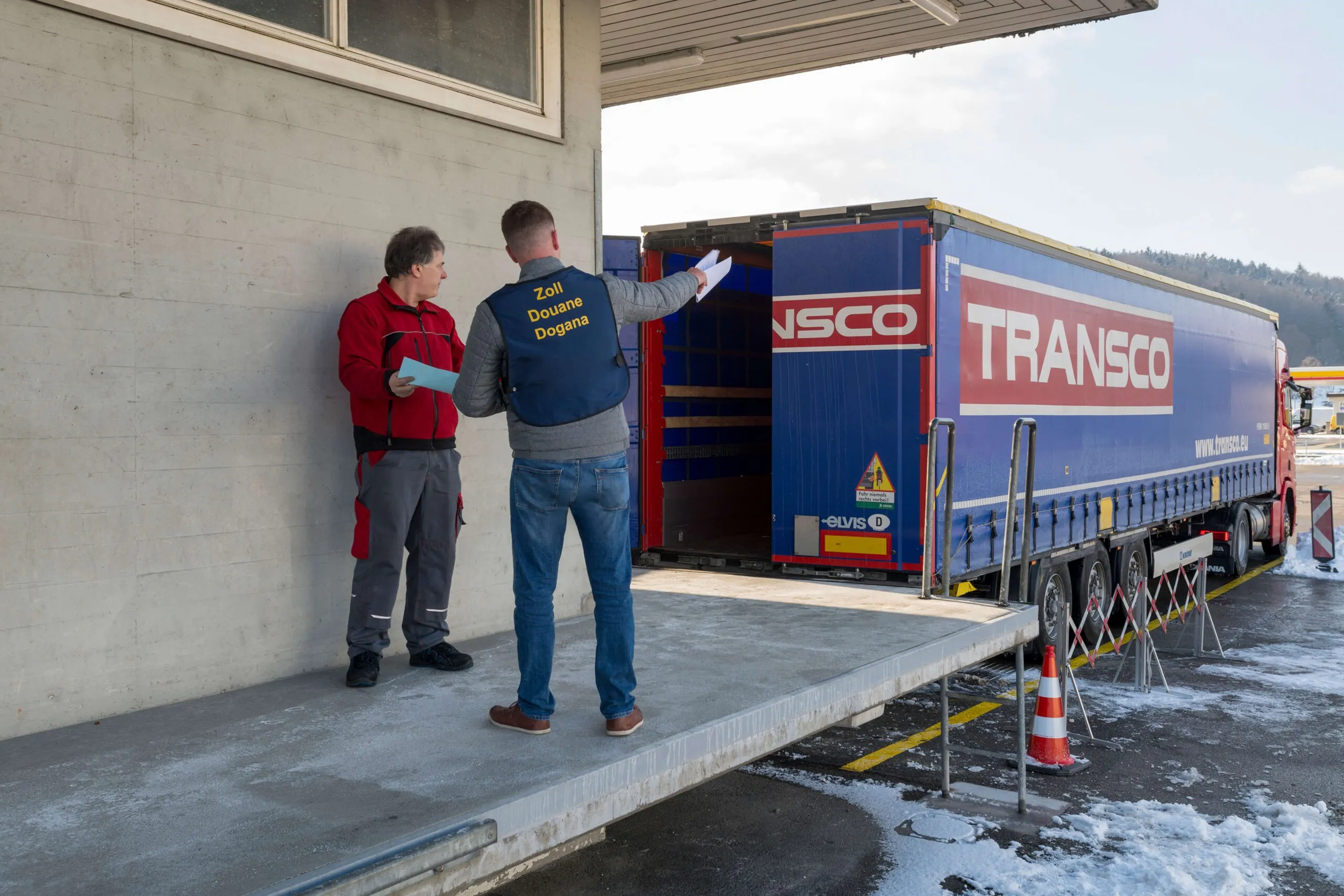 Mitarbeiter von Zoll und Spedition auf der Rampe vor einem Transco Lkw